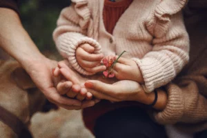 Mains d'enfants avec une fleurs dans les mains entouré de celles de ses parents.
