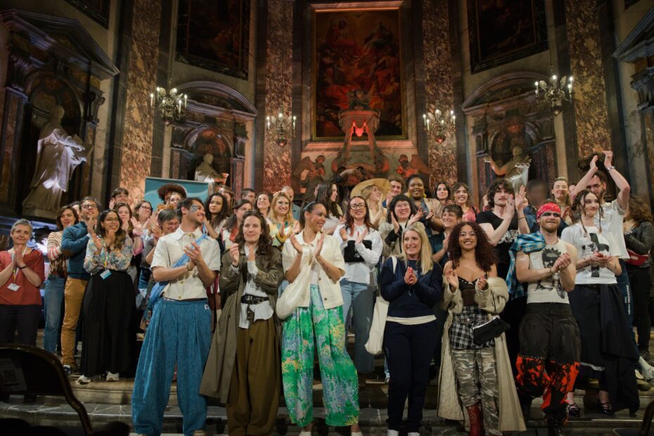 Photo représentant 16 modèles sur un escalier dans la nef d'une chapelle, avec du public sur les côtés.